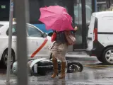 Una viandante se enfrenta a las fuertes rachas de viento mientras camina junto una moto volcada por una calle del centro de Madrid, .