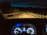 Un coche circula con las luces de largo alcance por una carretera convencional.