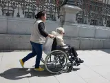 Una mujer mayor en silla de ruedas y su cuidadora pasean por el centro de Madrid.
