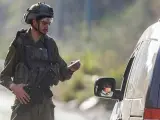 Un soldado israelí comprueba los teléfonos de los palestinos que pasan por un puesto de control militar israelí.