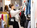Mujer joven de compras en el centro comercial junto a los estantes de ropa.