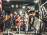 Dos peluqueros hacen el corte degradado a dos clientes.