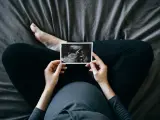 High angle shot of Asian pregnant woman holding an ultrasound scan photo in front of her baby bump, sitting on bed at home. Mother-to-be. Precious moment in life. Preparation for a new family member. Expecting a new life. Baby and new life concept