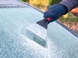 Un conductor quita con una rasqueta el hielo de su parabrisas.