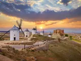 Wind mills and old castle in Consuegra, Toledo, Castilla La Mancha, Spain. Picturesque panorama landscape with road and view to ancient walls and windmills on blue sky with clouds.