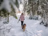 Una tutora junto a su perro paseando por la nieve.