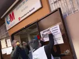 Dos hombres pegan carteles en la puerta del Centro de Salud por la falta de médicos.