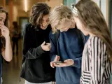 Varios niños miran un teléfono móvil en los pasillos de una escuela.