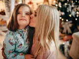 Una madre besa a su hija con discapacidad intelectual al lado del &aacute;rbol de Navidad.