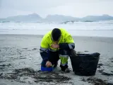 Un hombre recoge los pellets de plástico acumulados en la playa de Patos, en Nigrán, A Coruña.