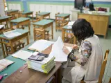 Una profesora corrigiendo exámenes en un aula de un centro educativo.