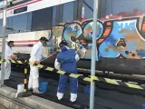 Operarios limpian un grafiti en un tren de Cercanías de Madrid.