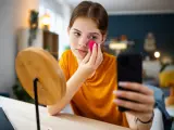 Adolescente enviando mensajes de texto en su teléfono mientras se maquilla.