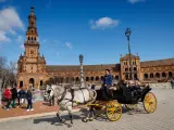 Turistas pasean a pie y en el tradicional coche de caballos este lunes por la Plaza de España de Sevilla