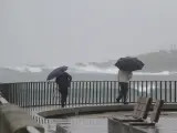 Tiempo lluvioso y varias personas que pasean por el paseo marítimo.