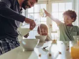 Un padre vierte leche de vaca en tazones para el desayuno de sus hijos.