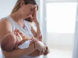 Una mujer, cansada y con tristeza sostiene a su bebé.