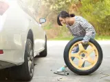 Una conductora cambiando la rueda pinchada de su coche.