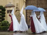 Nazarenos de la Hermandad de La Sentencia se protegen de la lluvia con paraguas en Córdoba.