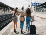 Three friends enjoying a trip together - Rear view. They are at a railroad train station.
