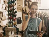 Una trabajadora autónoma con una tablet y hablando por el móvil en un taller de costura.