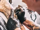 Tatuador haci&eacute;ndole un tatuaje en el brazo a un cliente.