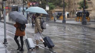 Una pareja con maletas se protegen de la lluvia bajo sus paraguas.