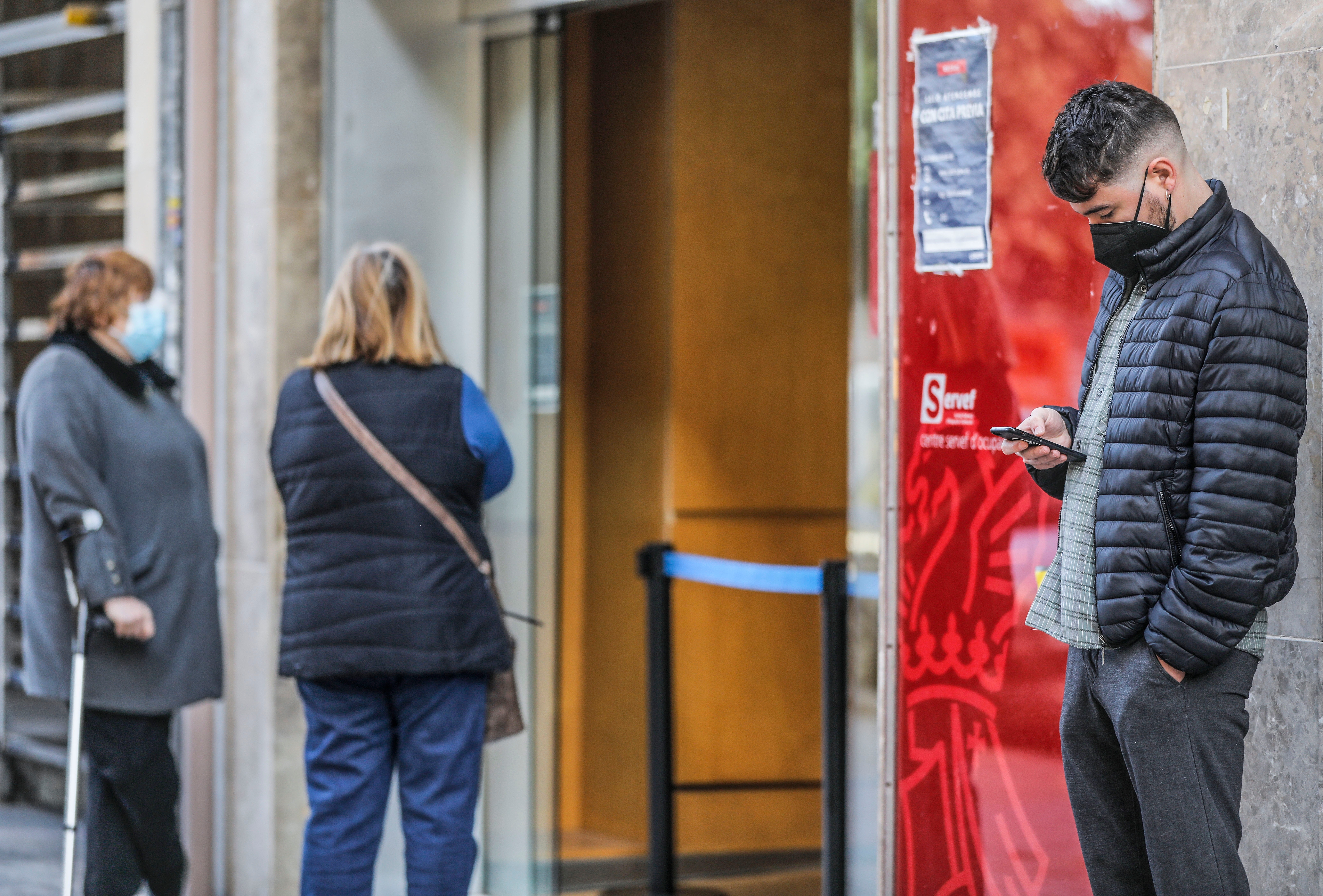 A young man looks at his mobile phone while waiting to enter a SEPE office in Valencia.