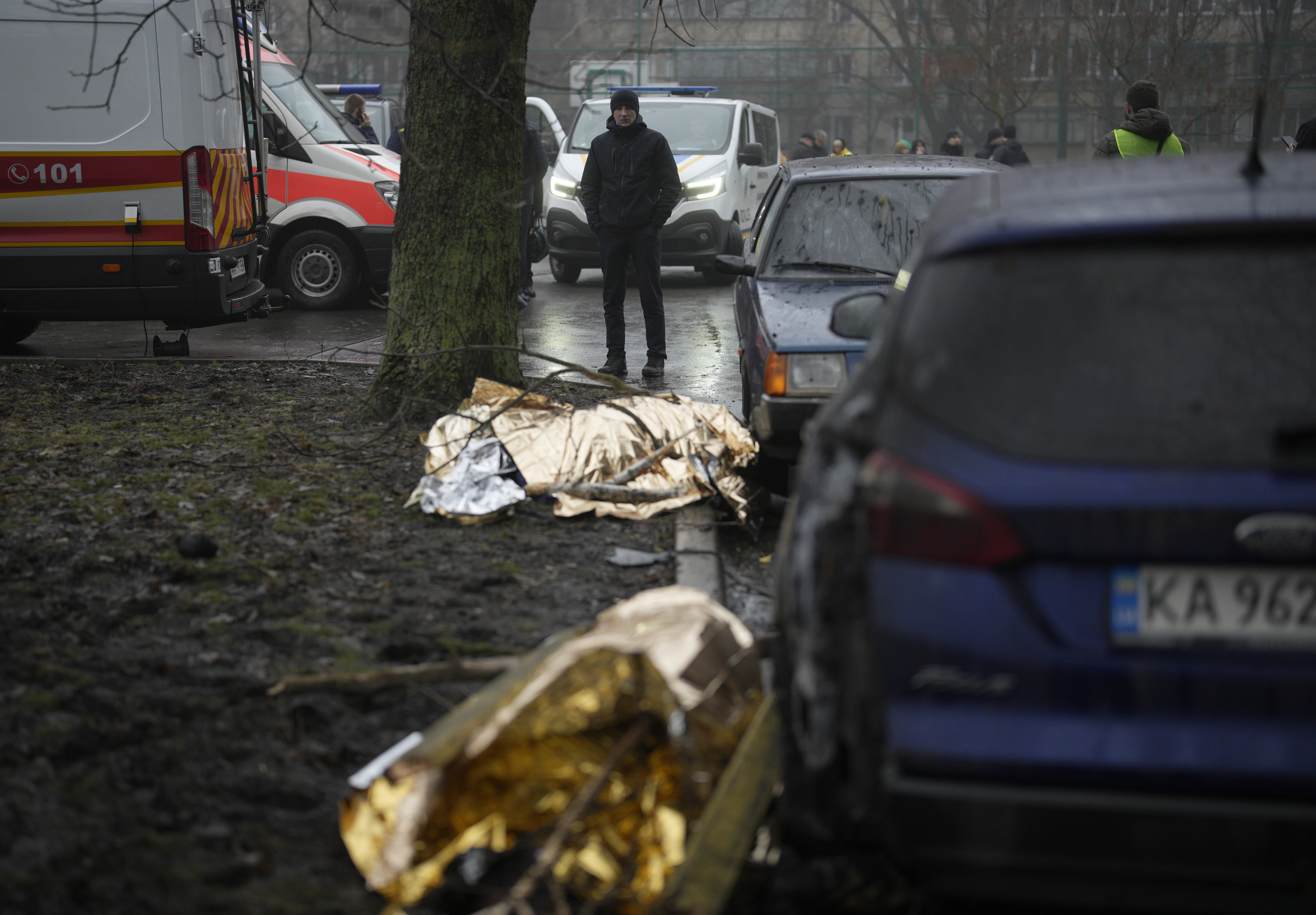 Un hombre mira los cuerpos cubiertos con mantas térmicas de dos de las víctimas del accidente de helicóptero que mató al ministro del Interior de Ucrania.