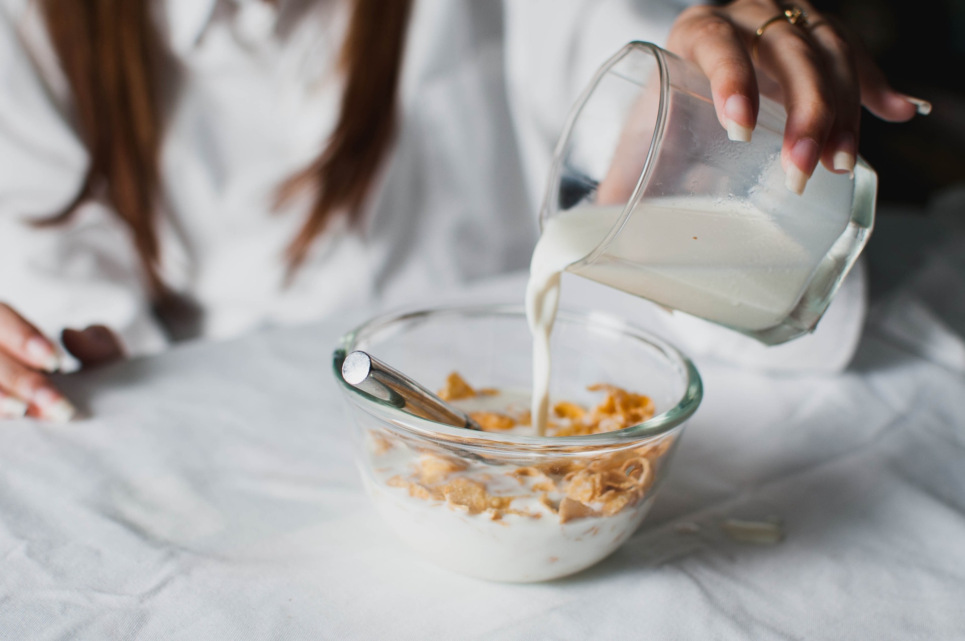 A woman prepares a bowl of cereal with milk for breakfast.
