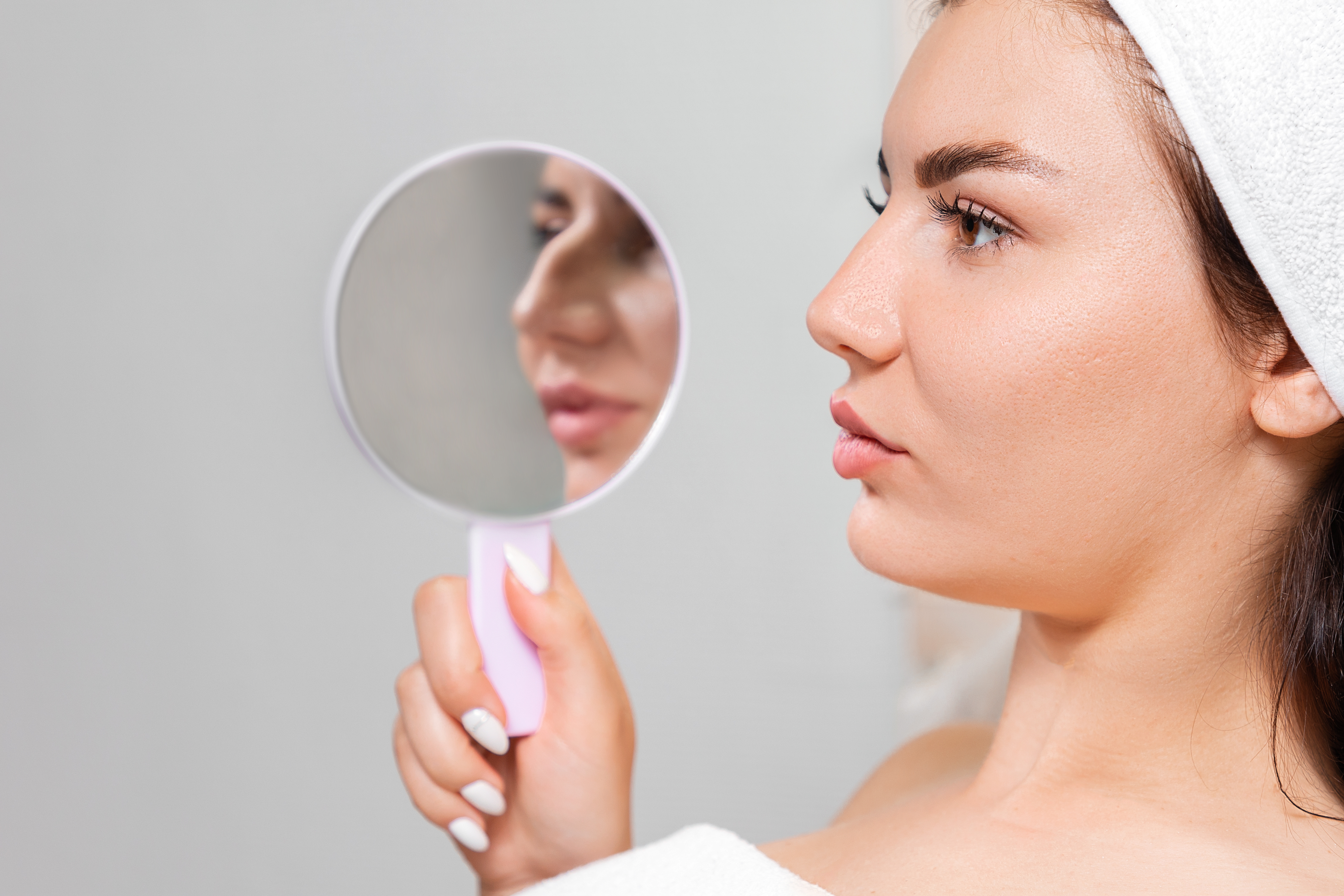 A woman holds a mirror with an aquiline nose.  Comparison of results before and after plastic surgery